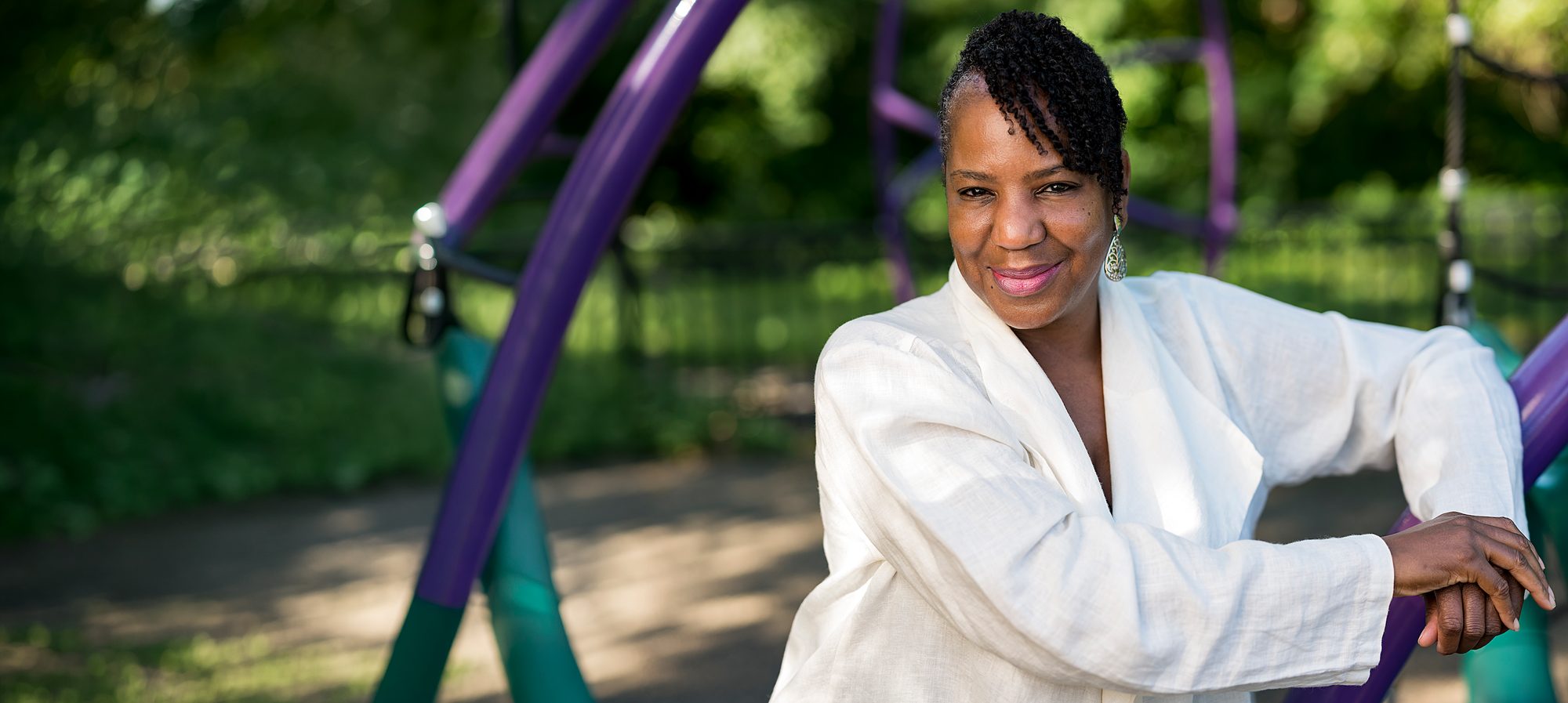 Author Caroline Brewer in a park, leaning on a purple play structure